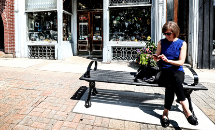 Woman sitting on street bench looking at her phone