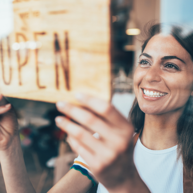 Young dark haired woman hanging an "open" sign in a window