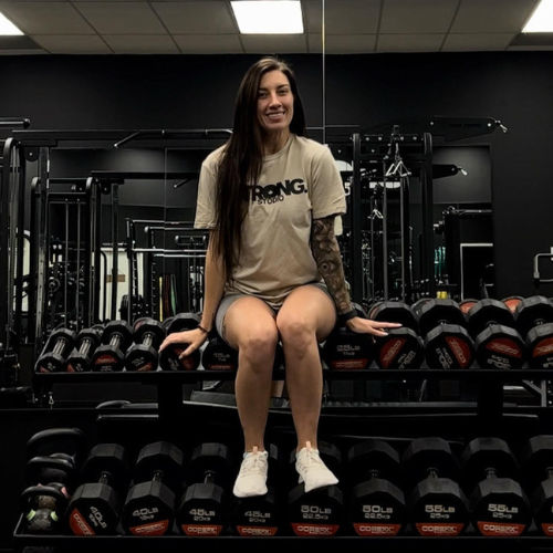 Strong Studio A woman sitting in a fitness gym on top of barbells