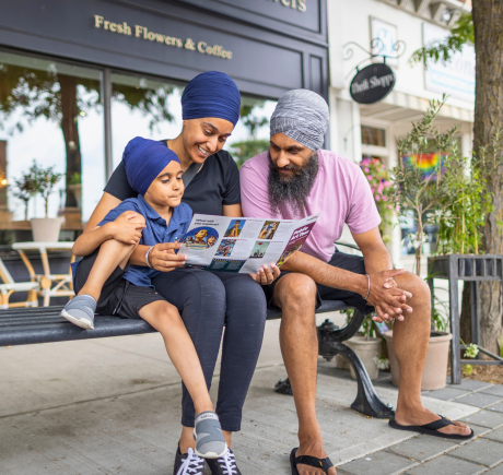 A Sikh family sits on a bench. They are looking at an art brochure.