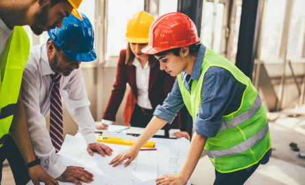 Construction workers are looking down at a plan on a table.