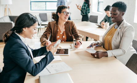 Three business women are sitting around a table talking.