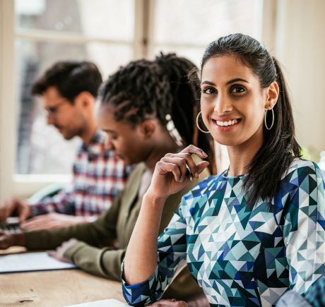 An Indian woman is sitting a table with an open notebook. There is a woman and a man beside her.