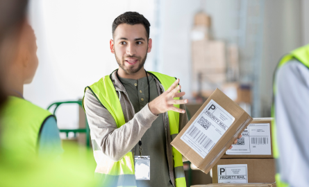 A man is holding a shipping box and instructing other employees