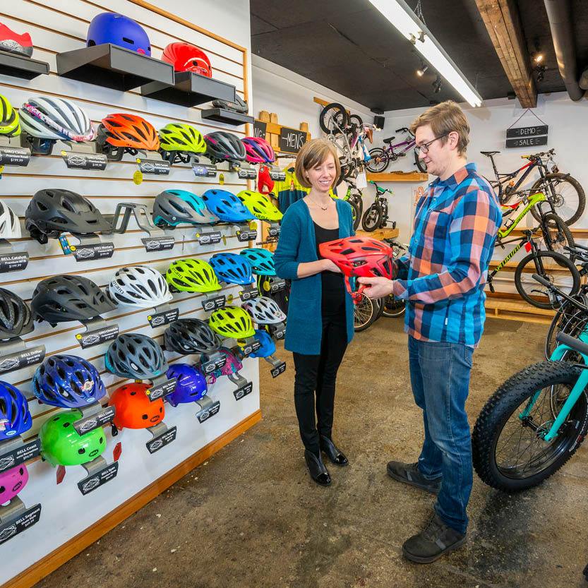 A man and a woman standing in a bicycle shop discussing helmets