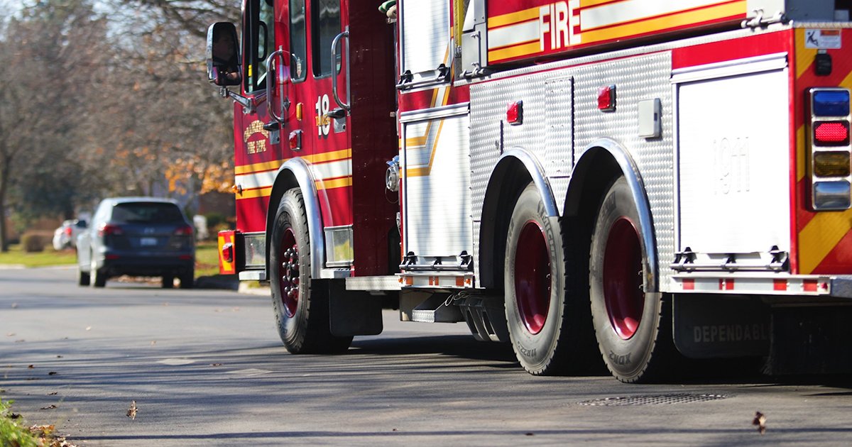 A fire truck passes down a residential street with vehicles parked on just one side.