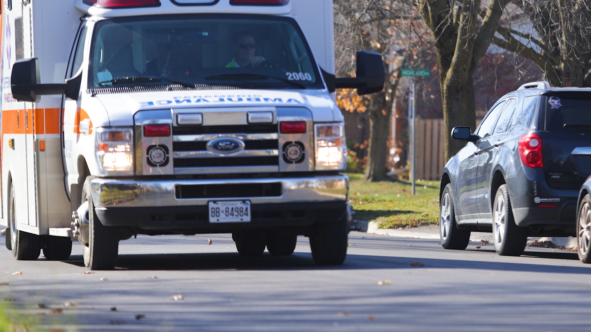 An ambulance passes down a street with vehicles parked on one side only.