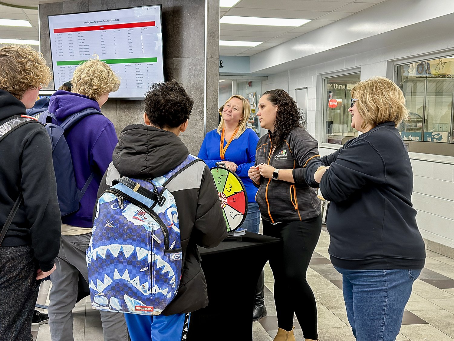 Students stand in front of a trivia wheel while  talking to Orangeville Recreation staff