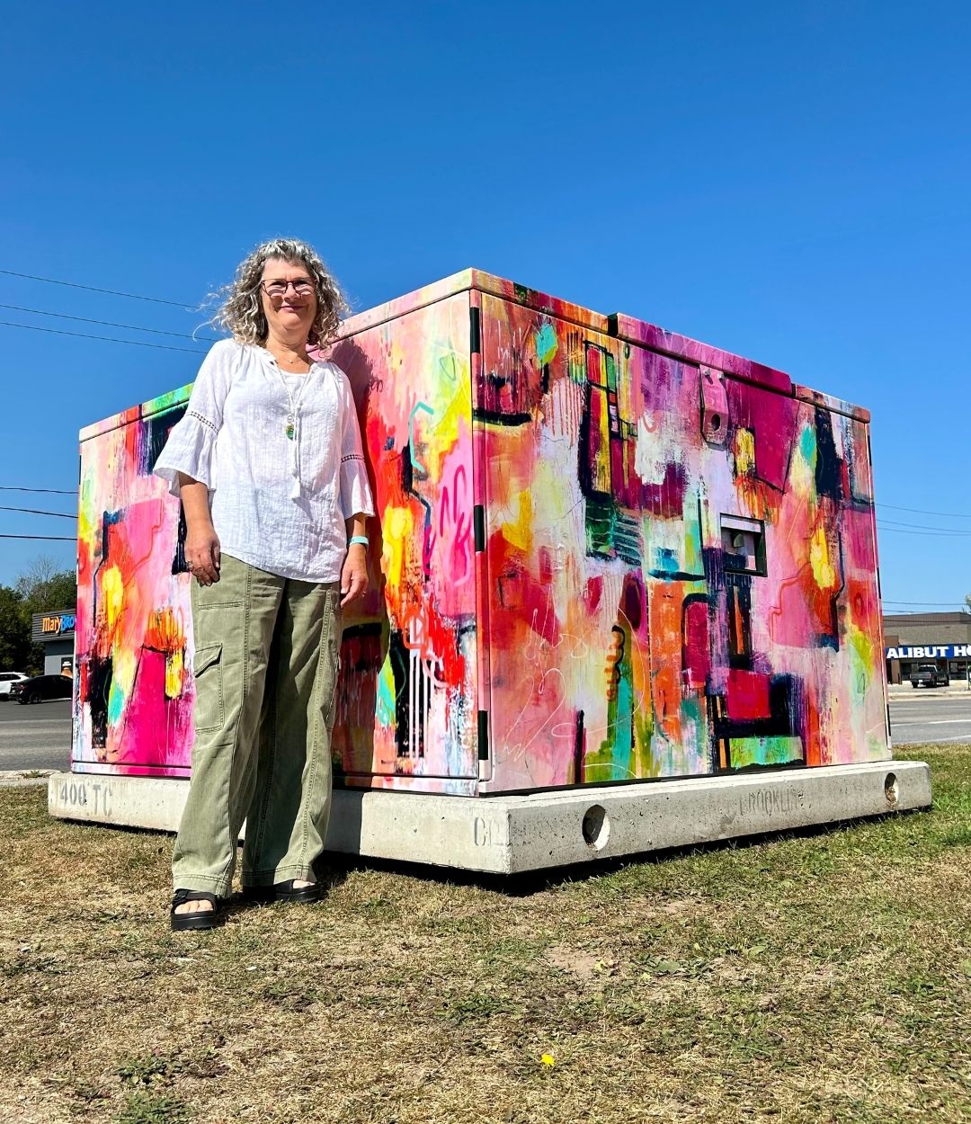 A woman standing in front of a Hydro transformer covered in colourful artwork