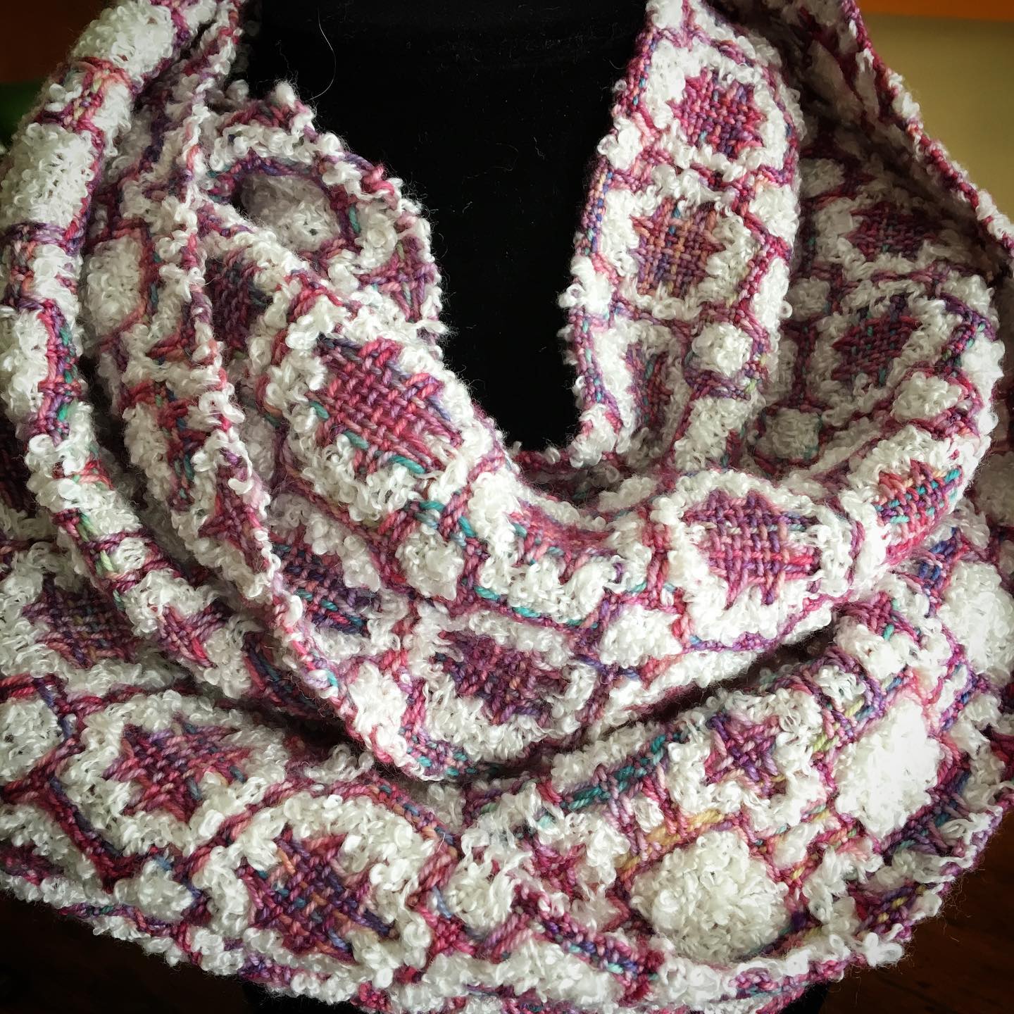 A woven scarf with hues of white, pink and purple wrapped around a dress form