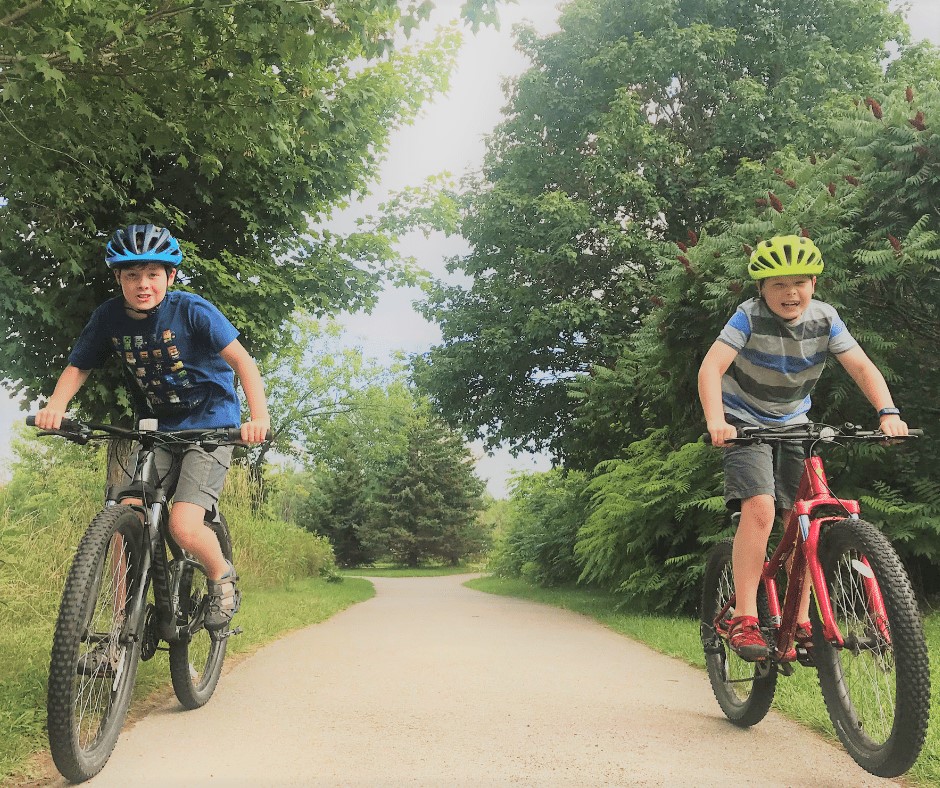 Two boys riding bikes on a tree-lined path