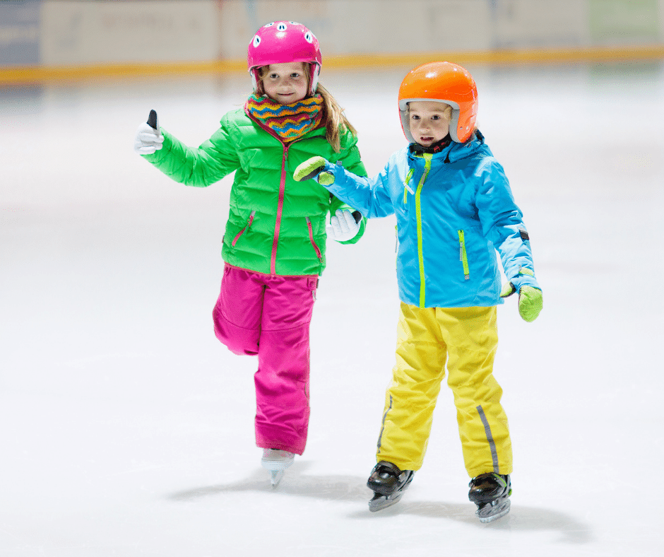 Two young children ice skating inside an arena.