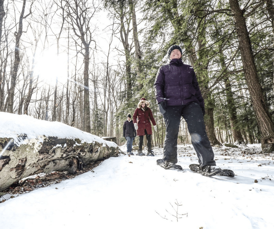 Three women dressed in winter jackets and snowpants snowshoeing on a forested winter trail