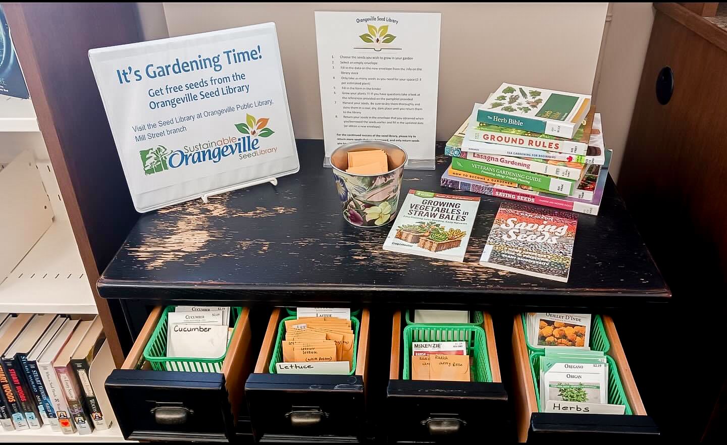 A picture of a seed library set up on an old library card filing desk. Seed envelopes are in the drawers with labels on them, with books, a binder, and a sign on top of the desk.