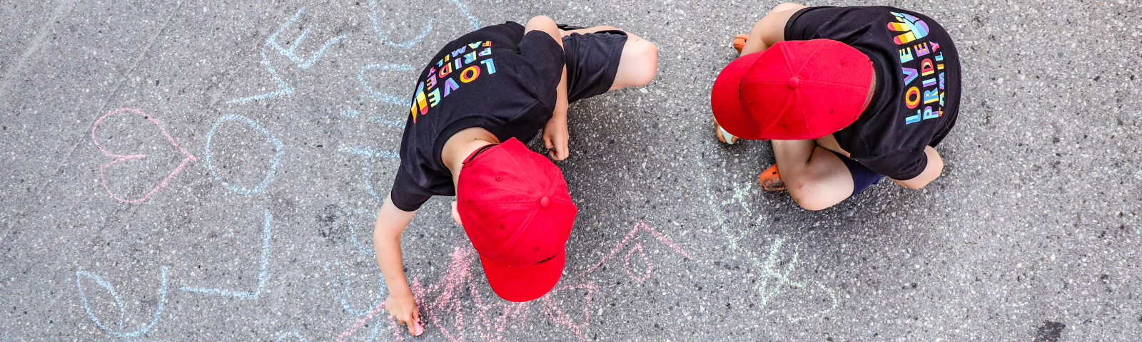 Overhead view of two children drawing on pavement with chalk