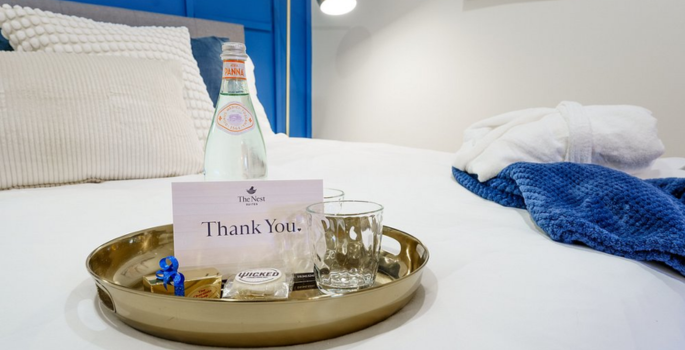 A hotel bed with a bright blue headboard and a tray with bottled water and cookies.