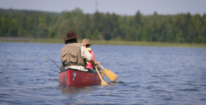 A father and daughter paddle a canoe in a lake.