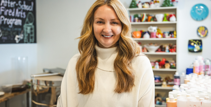 A woman smiles while standing in front of hand-made pottery