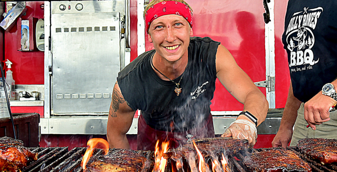 A man smiles as he grills ribs at a festival