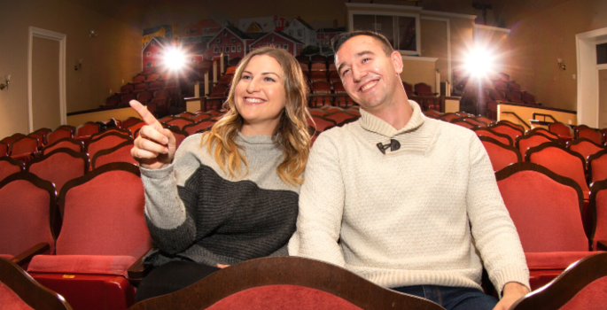 A man and woman smile as they point toward the stage in a theatre