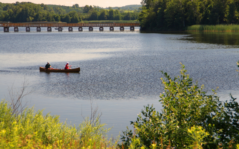 Two people in a canoe on a lake with a boardwalk behind them