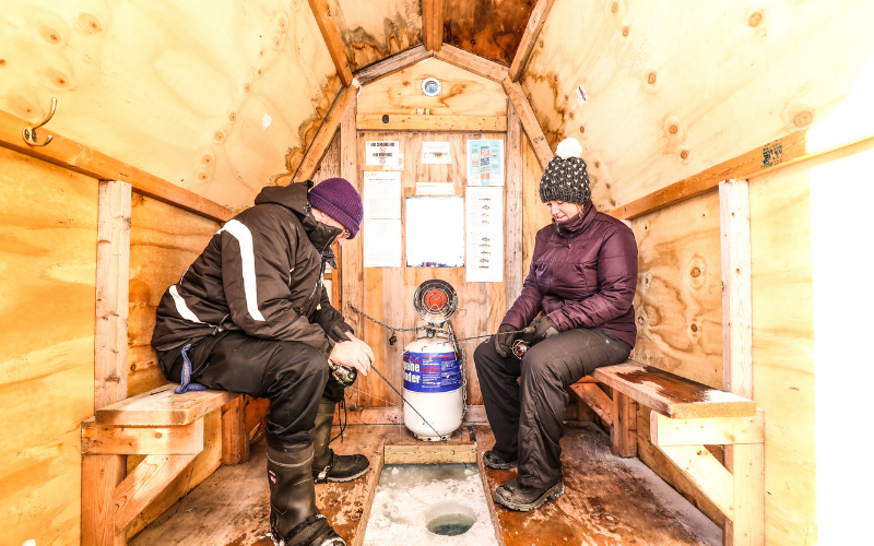 Two people ice fishing in a wooden hut