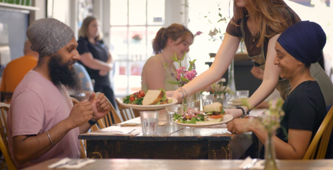Pia's on Broadway a couple eat lunch at a harvest table in a small restaurant