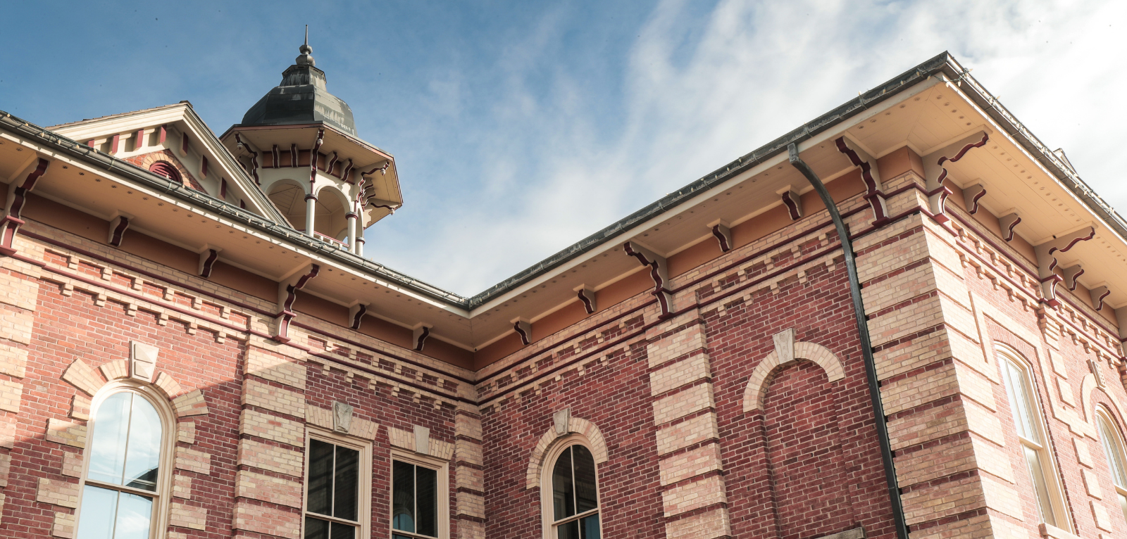 A brick historic building with a cupola sits in front of a blue sky. 